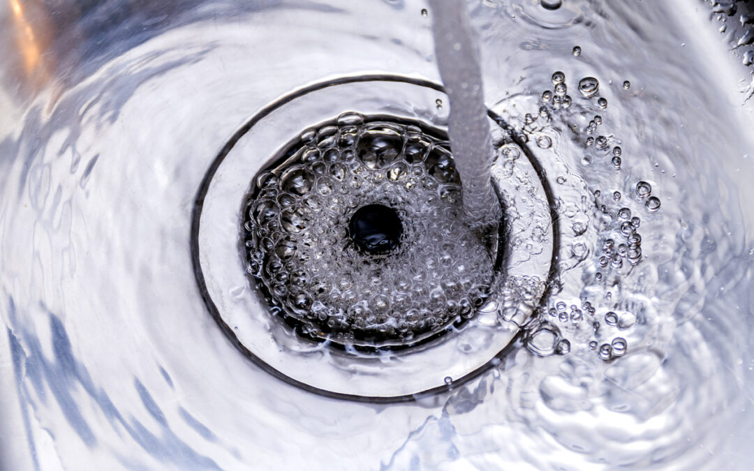 A stream of clean water flows into the stainless steel sink. Sink plug hole close up macro to show drain cleaning services